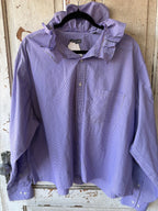 A lavender and white micro-checkered long-sleeve button-up shirt with a ruffled collar, hanging on a black hanger against a rustic, weathered wooden door.