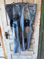 Light blue denim jeans with multiple colorful patchwork fabric patches and distressed details, hanging on a wooden door.