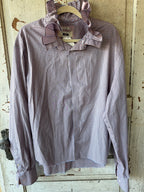 A long-sleeve button-up shirt with a pink and blue gingham check pattern and a ruffled collar, hanging on a wooden hanger against a distressed white wooden door.