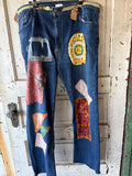 A pair of blue denim jeans with multiple colorful patchwork fabric appliques and a distressed patch on the thigh, hanging on a wooden door.