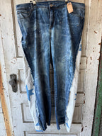 Distressed blue denim jeans with a white quilted patch featuring a blue star on each leg, hanging on a wooden door.