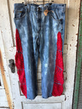 Light blue acid-wash denim jeans with bright red crochet lace panels on the lower legs, hanging on a metal hanger against a distressed white wooden door.
