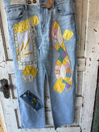 Light blue denim jeans with extensive handcrafted patchwork appliques, including a large multicolor patchwork bow on the thigh, a wheat field design on the pocket area, and a small floral patch near the lower leg, displayed against a distressed white wooden door.