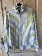 A long-sleeve button-up shirt with vertical stripes in light blue, green, and white, hanging on a black hanger against a rustic, weathered wooden door.