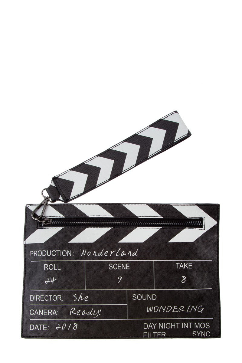 A black and white faux leather clutch designed like a film clapperboard, featuring a wrist strap and printed details including 'Production: Wonderland'.